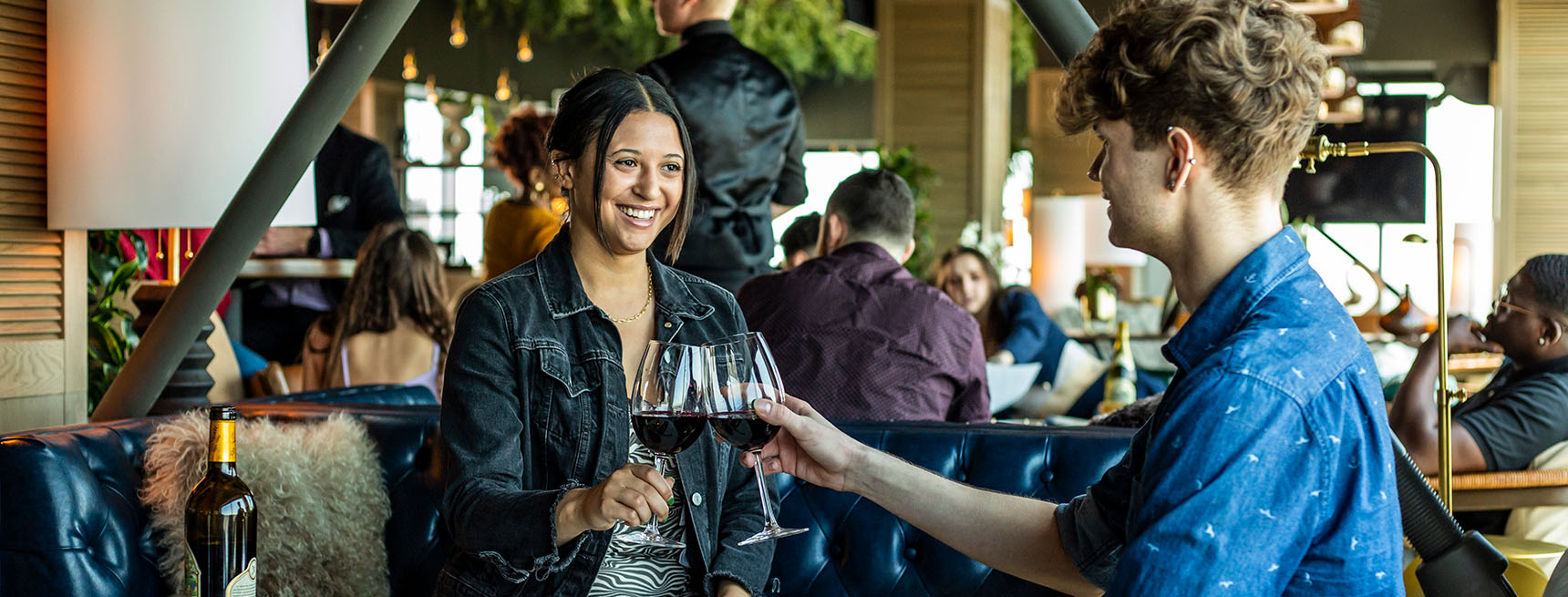 Couple seated in lounge clinking glasses of red wine.